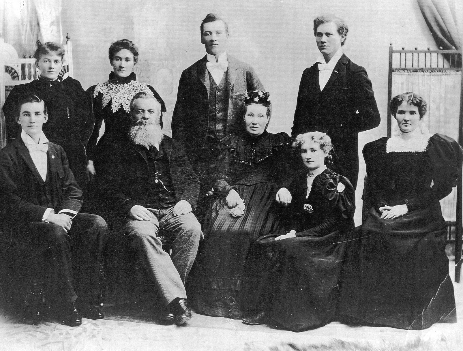 Nine members of the McConnell family posing for a family portrait. The women are wearing long long dresses with puffy sleeves, the men are in suits, vests and bowties.