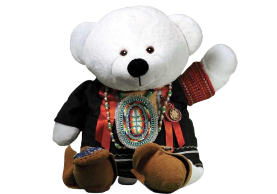 Spirit Bear est une peluche d'ourson qui est habillé dans un habit tradition autochtone; il porte des mocassins et salue de sa patte gauche.