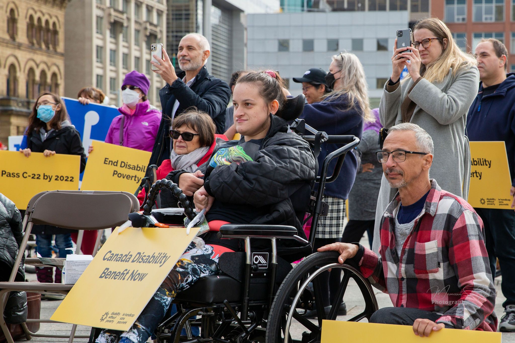 A woman in a wheelchair and other peoples of mixed abilities hold protest signs saying Canada Disability Benefit Now outside Parliament