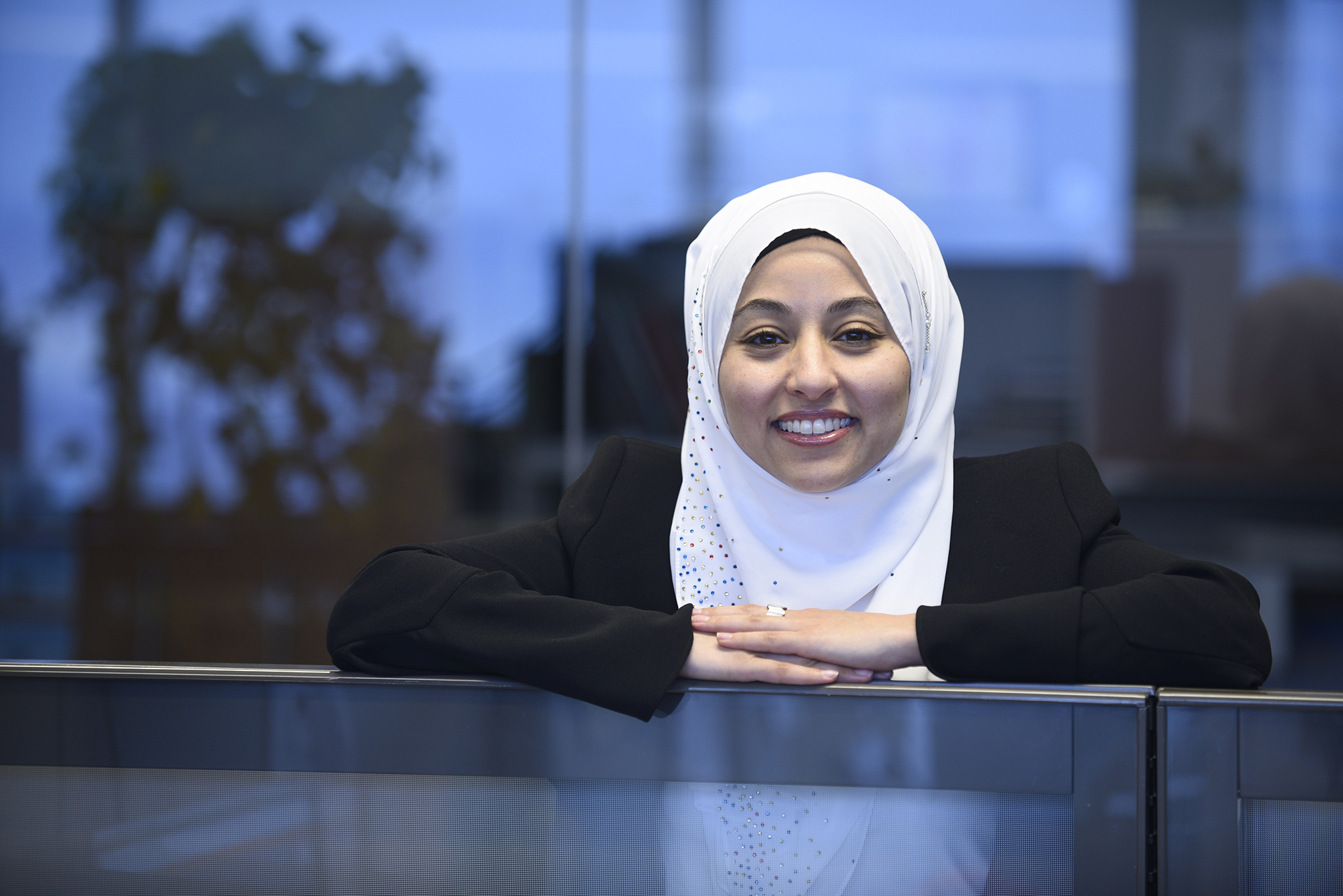 Hager Osman porte un hijab orné de bijoux et s'appuie des deux bras sur le bord supérieur d'un bureau. 