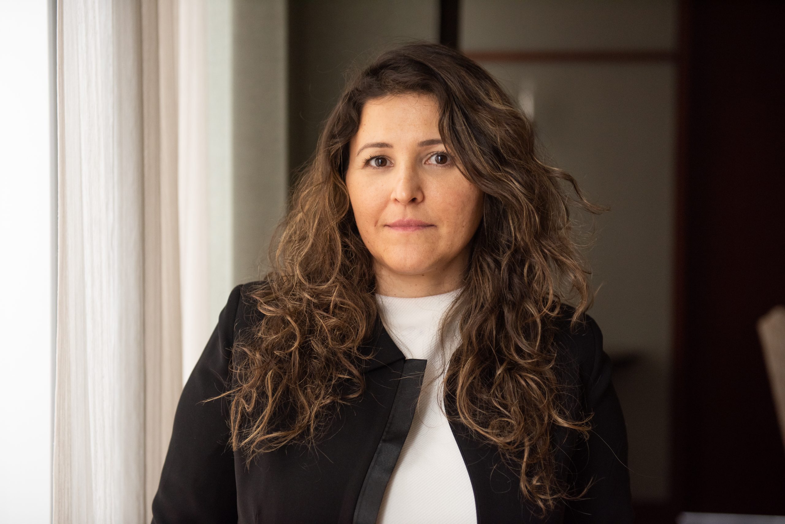 Katia Haddad's curly brown hair billows down over her black blazer and white shirt.