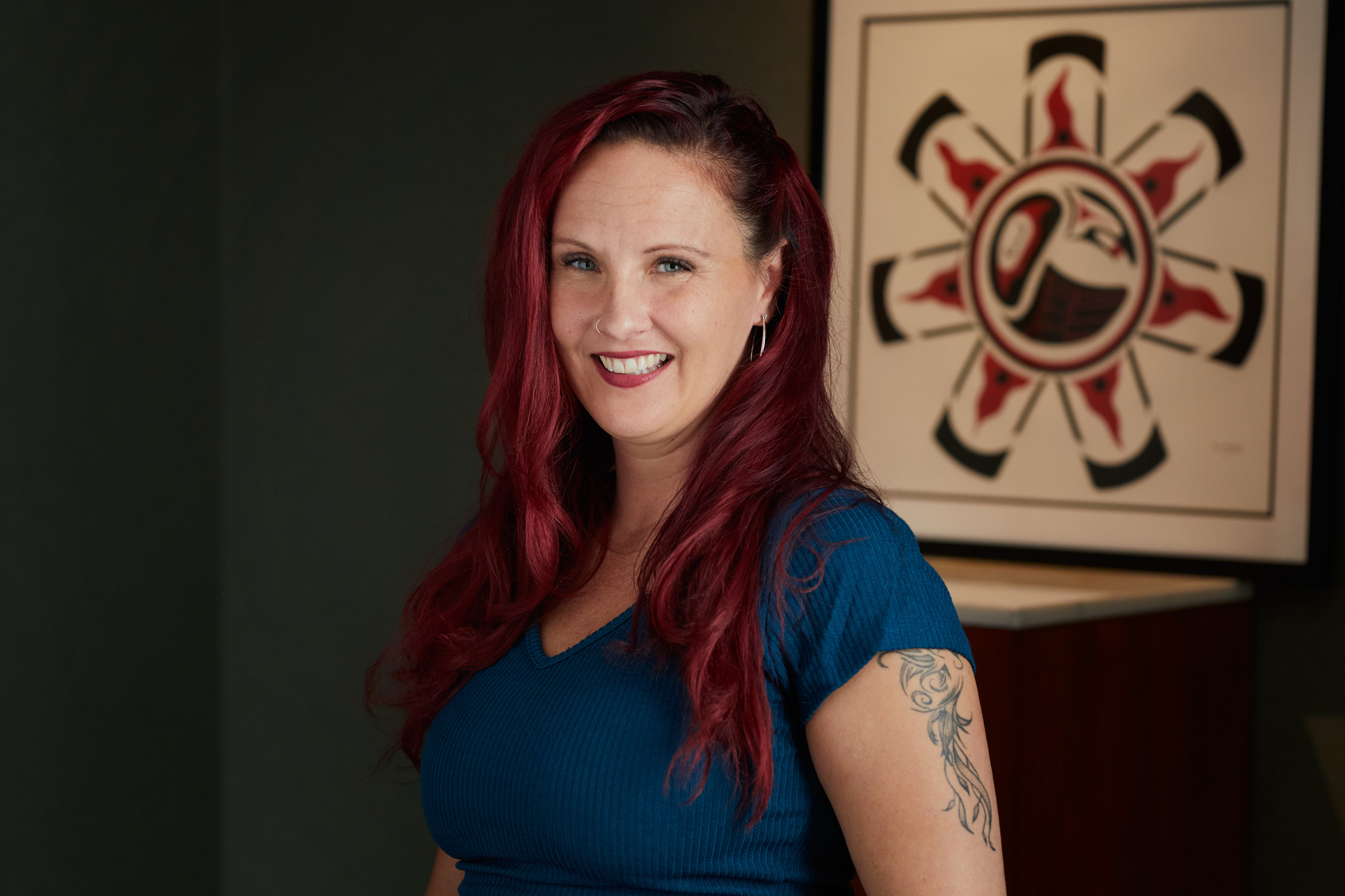 Photo of Naomi Graham, in the background a photo of an Eagle in red, black and white, in the Haida Nation type of iconography, with 7 feathers around a circle.